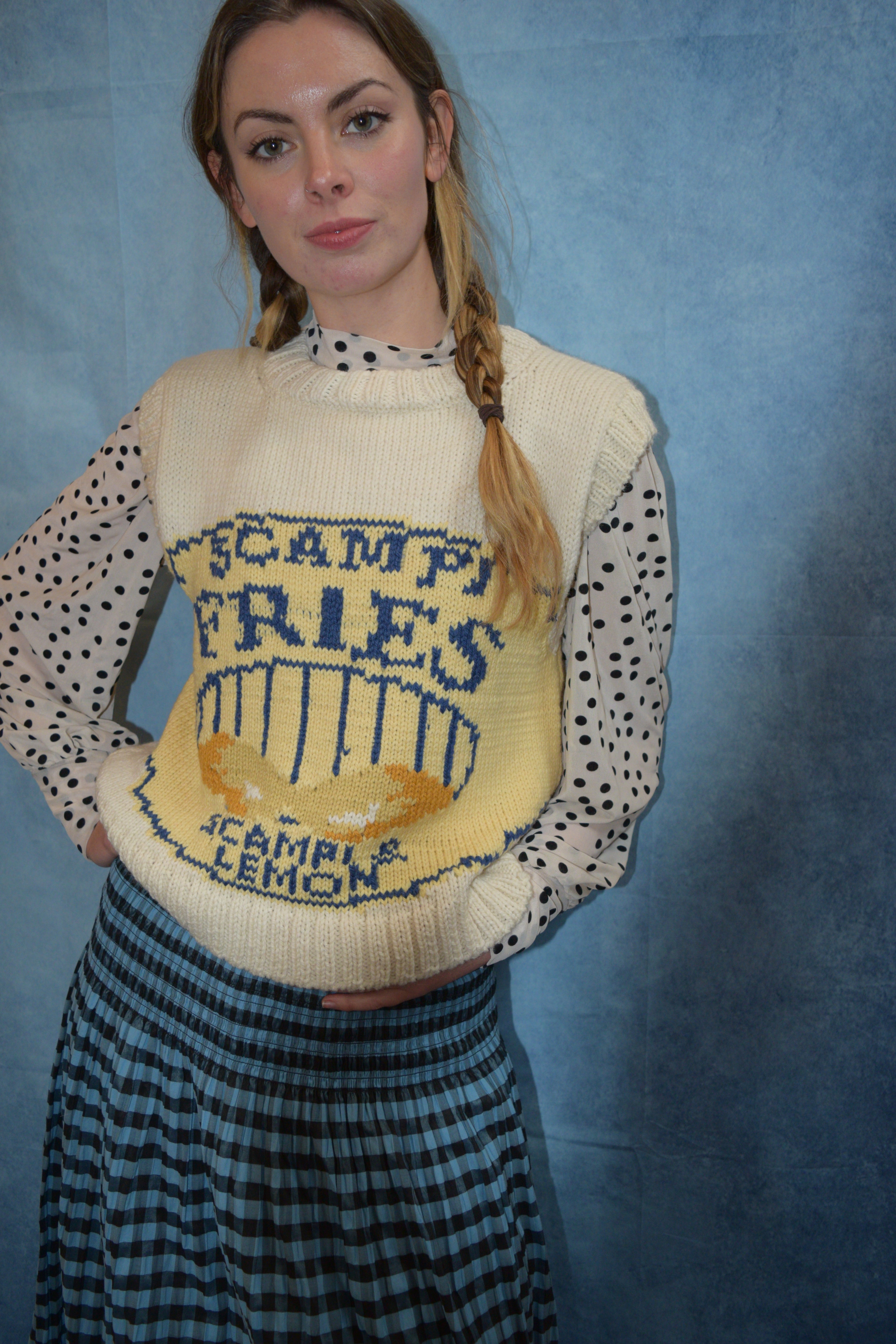 Person wearing a polka dot shirt and a sweater with a visible brand logo on a blue background