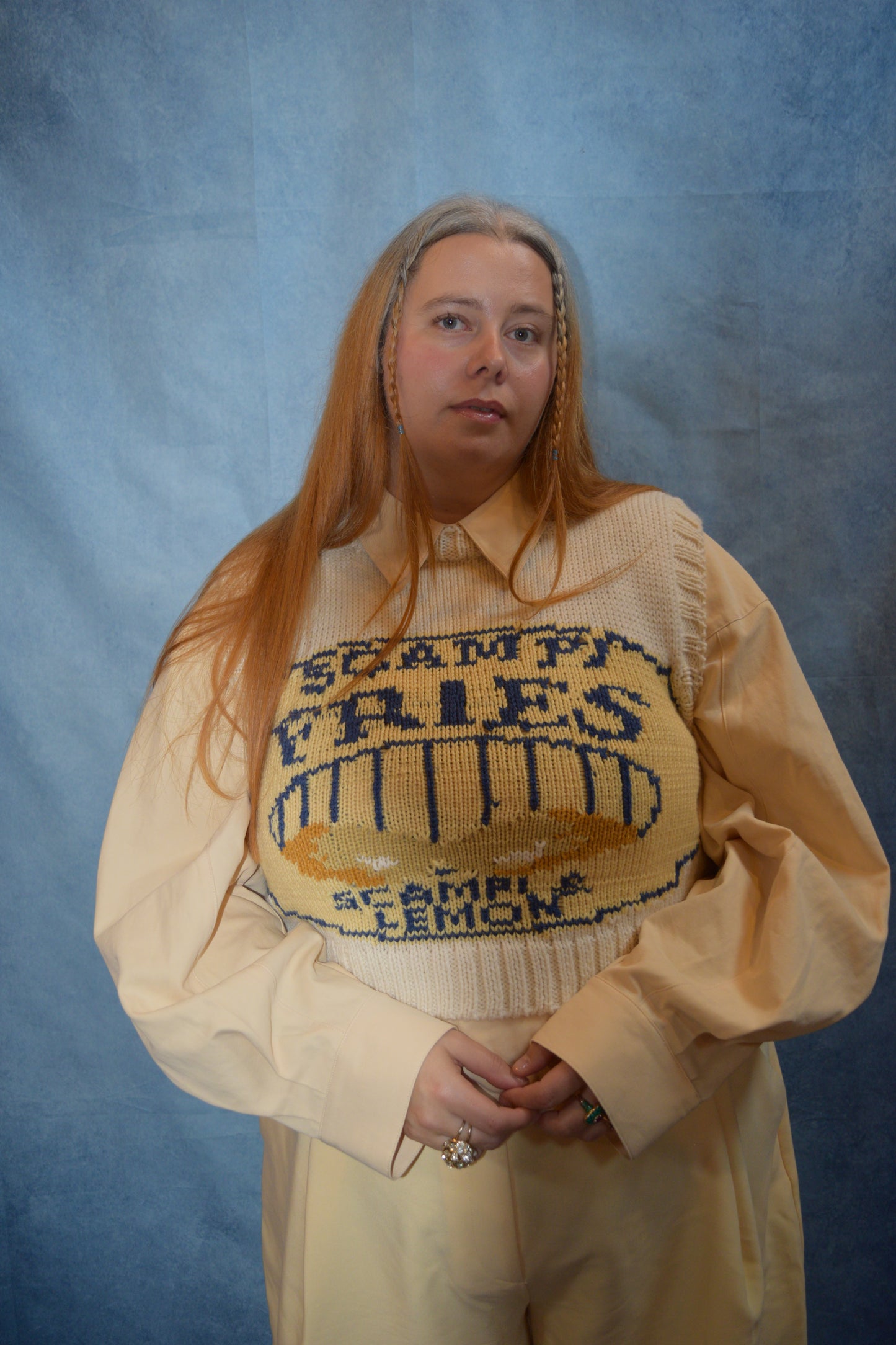 Person wearing a beige sweater with text and a yellow bag on a blue background