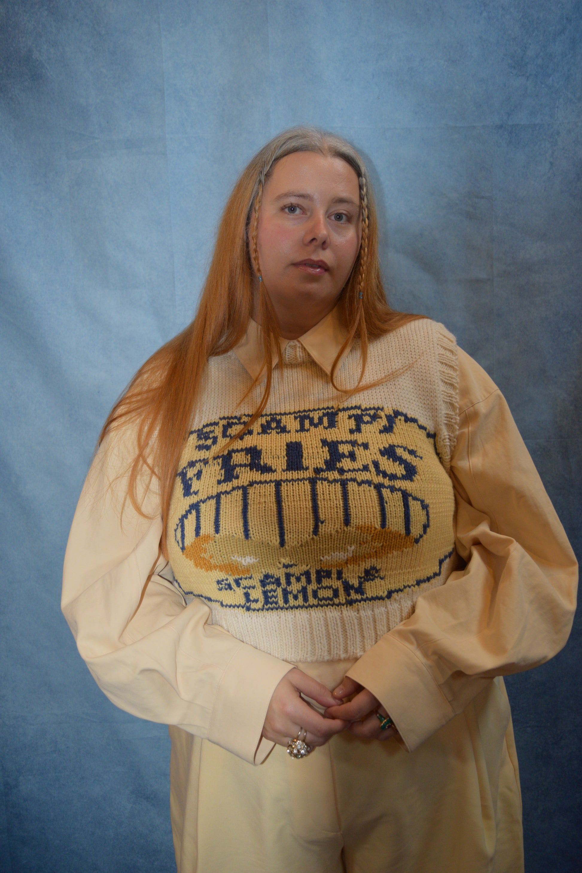 Person wearing a beige sweater with text and a yellow bag on a blue background